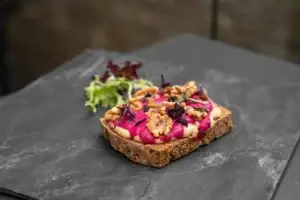 Veganer offener dunkler Toast mit Hummus und Grillgemüse