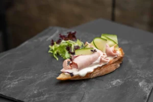 Belegtes Brötchen mit aufgeschlagenem Frischkäse, Schinken und Gurke